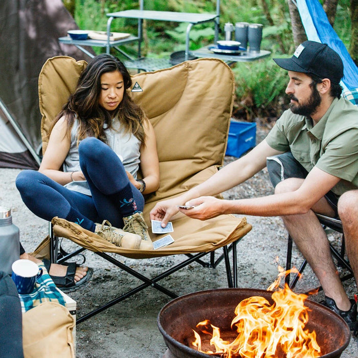 A man handing out cards to a woman sitting on the Woods Mammoth Folding Padded Camping Chair in Dijon around a campfire on campground