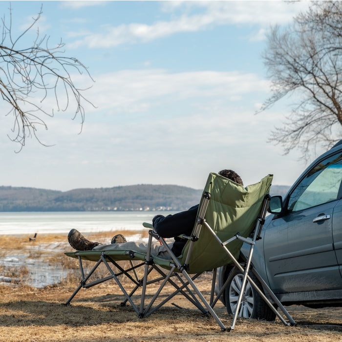 Back view of a person relaxing on the Woods Ashcroft Camping Lounger Chair in Sea Spray next to a car