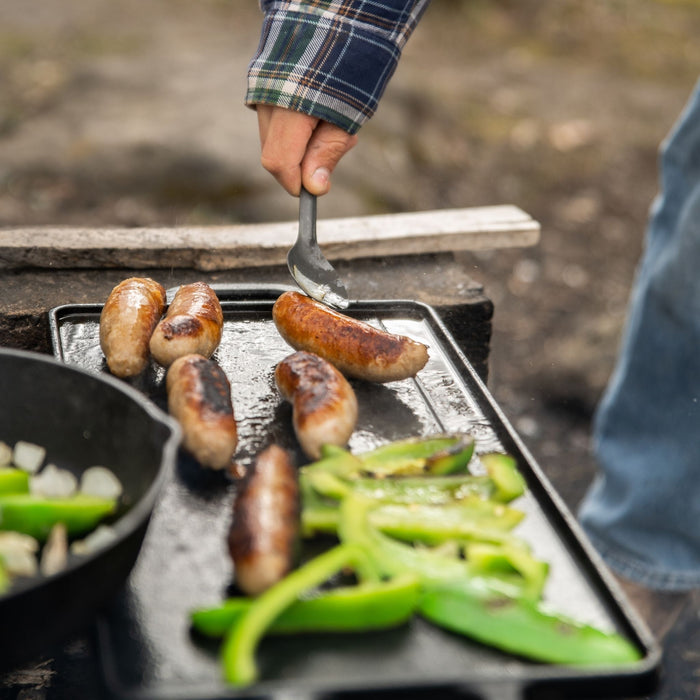 Close up side view of sausages and vegetables cooking on the Woods Heritage griddle 