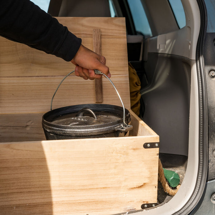 A person taking out the Dutch oven from wooden crate inside a car trunk