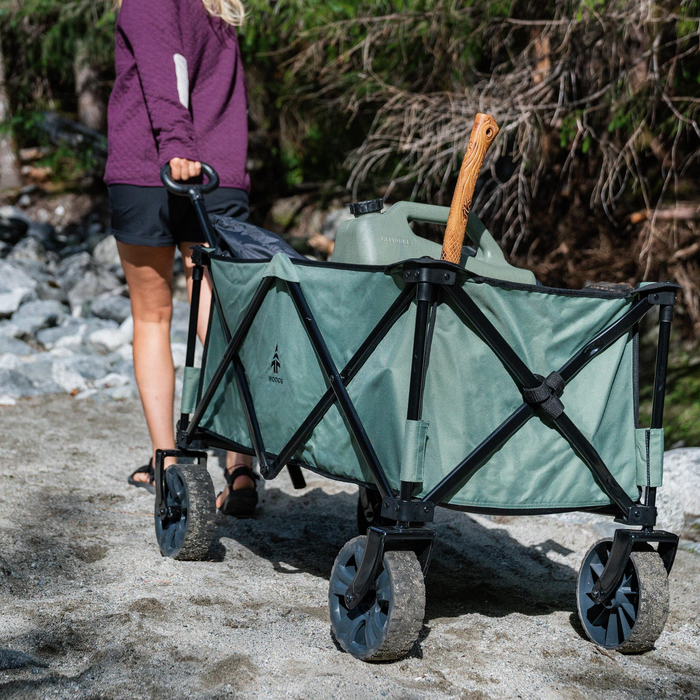A person rolling the Woods Outdoor Collapsible Utility King Wagon in Sea Spray filled with gear on sand