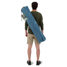 Load image into Gallery viewer, Behind view of a person carrying the Woods Siesta Folding Reclining Padded Camping Chair in Blue inside carry bag across their back