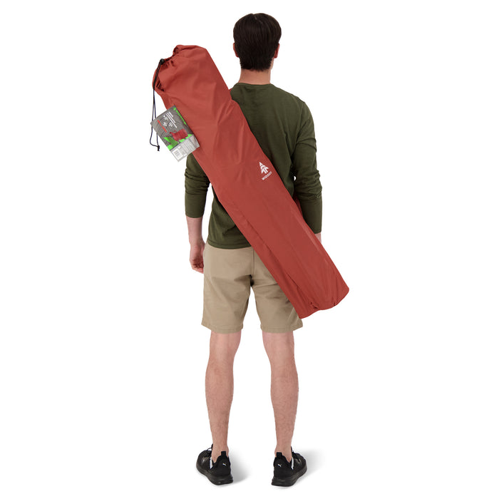 Behind view of a person carrying the Woods Siesta Folding Reclining Padded Camping Chair in Red inside carry bag across their back
