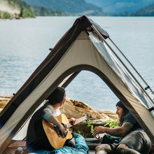 Load image into Gallery viewer, Two people relaxing inside the Woods A-Frame 3-Person 3-Season Tent in Brown on a campground near the water