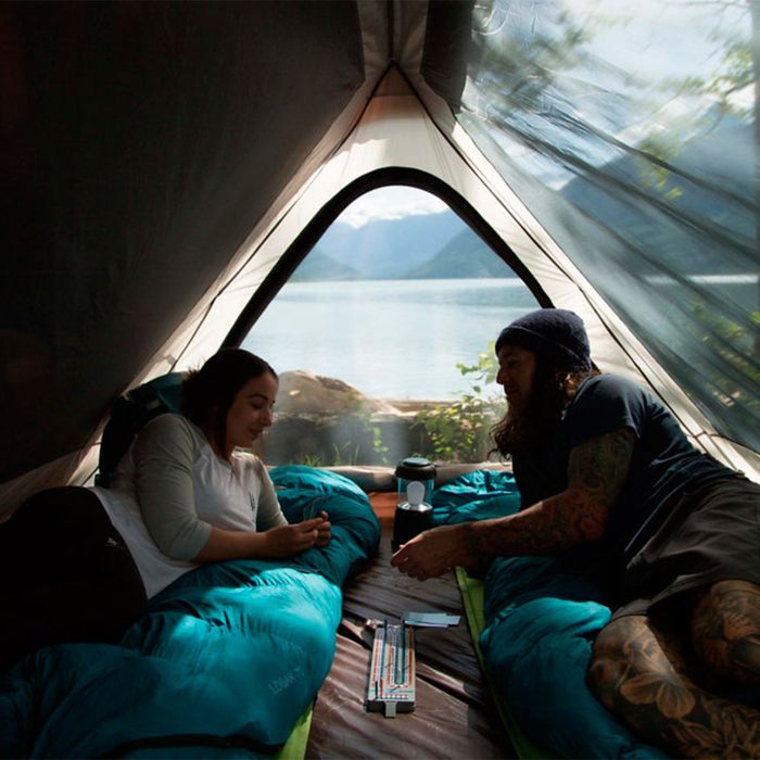 Two people playing cards inside the Woods A-Frame 3-Person 3-Season Tent on a campground near the water
