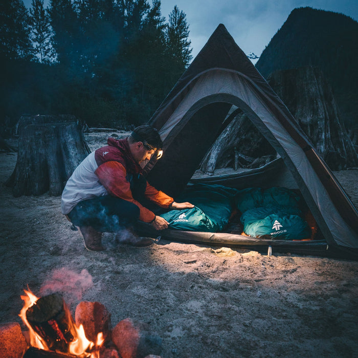 A person adjusting their sleeping bag by the Woods A-Frame 3-Person 3-Season Tent on a campground