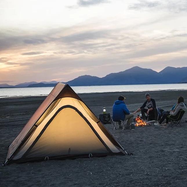 Three people surrounding a campfire set up next to the Woods A-Frame 3-Person 3-Season Tent