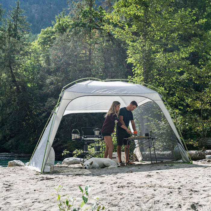 Two people cooking under the Woods Easy Setup Canopy Camping Screen House on campground