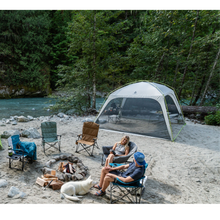 Load image into Gallery viewer, Two people lounging on camp chairs in front of the Woods Easy Setup Canopy Camping Screen House on campground