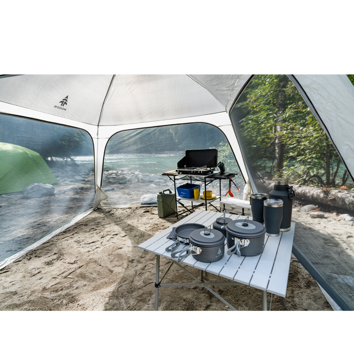 Various cookware and camping tables set up under the Woods Easy Setup Canopy Camping Screen House on campground