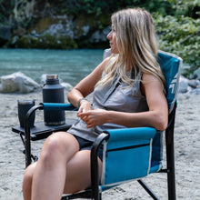 Load image into Gallery viewer, A woman sitting on the Woods Folding Directors Camping Chair with Table in Blue on campground