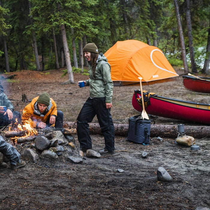 Two people around a campfire with canoes and the Woods Pinnacle Lightweight 2-Person 4-Season Tent in the distance