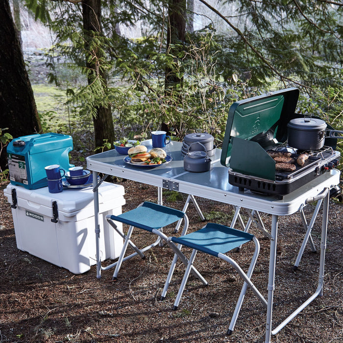 Woods Selkirk Anodized 4-piece Camping Cook Set with other dishware and portable stove on top of a camping table on campground
