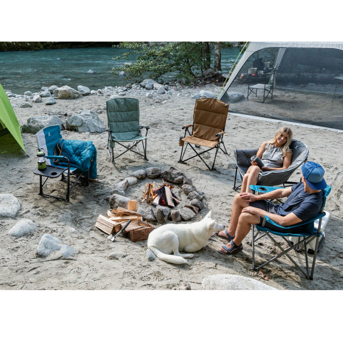 Two people sitting on camping chairs with three other chairs around a campfire on campground
