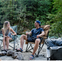 Load image into Gallery viewer, Two people sitting on Woods Folding Padded Camping Chairs around a campfire 